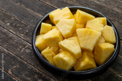 Pineapple chunks in a bowl on a rustic wooden table.