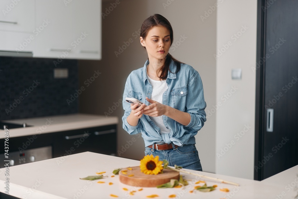 Beautiful Young Caucasian Female Standing in Modern Kitchen, Holding a Salad, Smiling and Talking on Mobile Phone