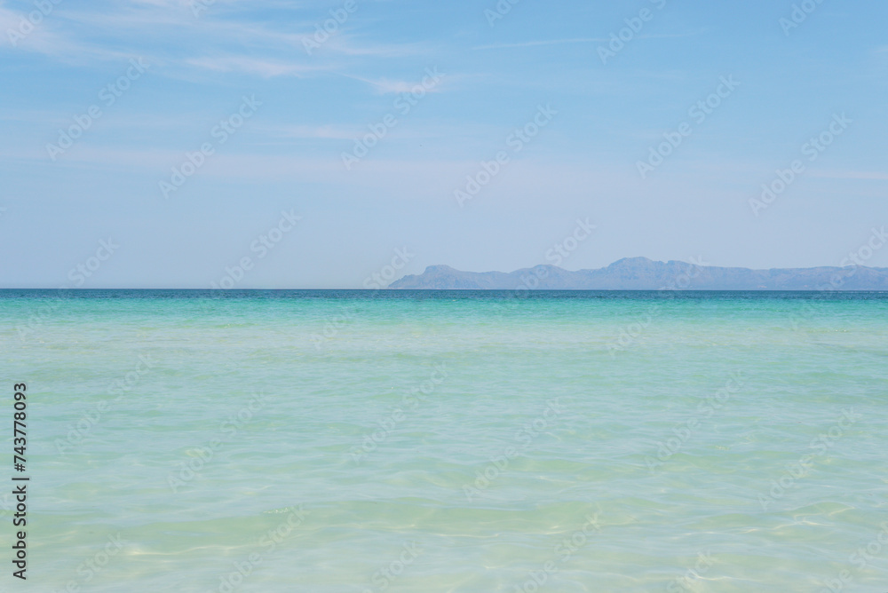 A gorgeous beach with super clear, turquoise water. Mountains in the distance. Sunny weather with a bright blue sky. Alcudia, Majorca. 