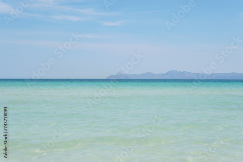 A gorgeous beach with super clear, turquoise water. Mountains in the distance. Sunny weather with a bright blue sky. Alcudia, Majorca. 