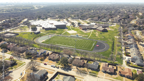 Middle school football stadium with artificial turf, yard markings, track and field situated in upscale residential neighborhood outside Dallas, Texas, lake and highway in distance background