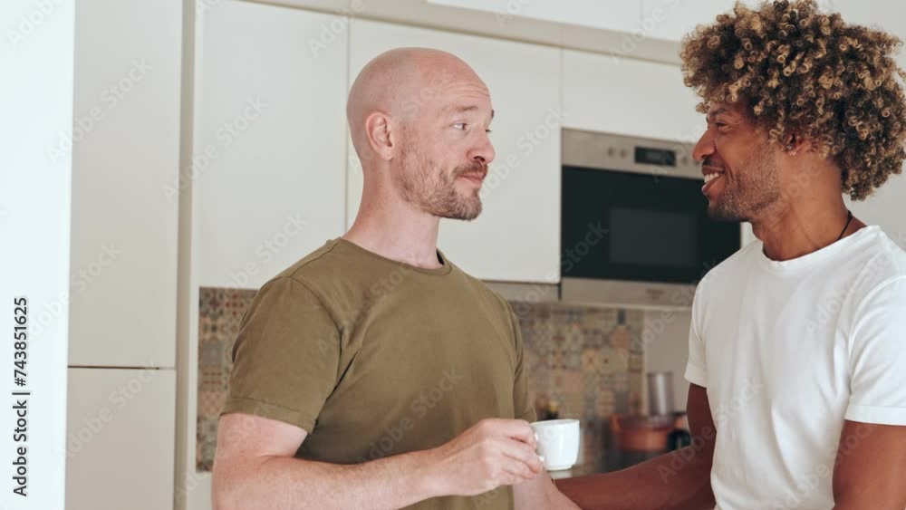 A loving gay couple shares a moment of happiness in the kitchen. They are smiling and engaged in a relaxed morning conversation. A loving gay couple shares a moment of happiness in the kitchen. They are smiling and engaged in a relaxed morning conversation.