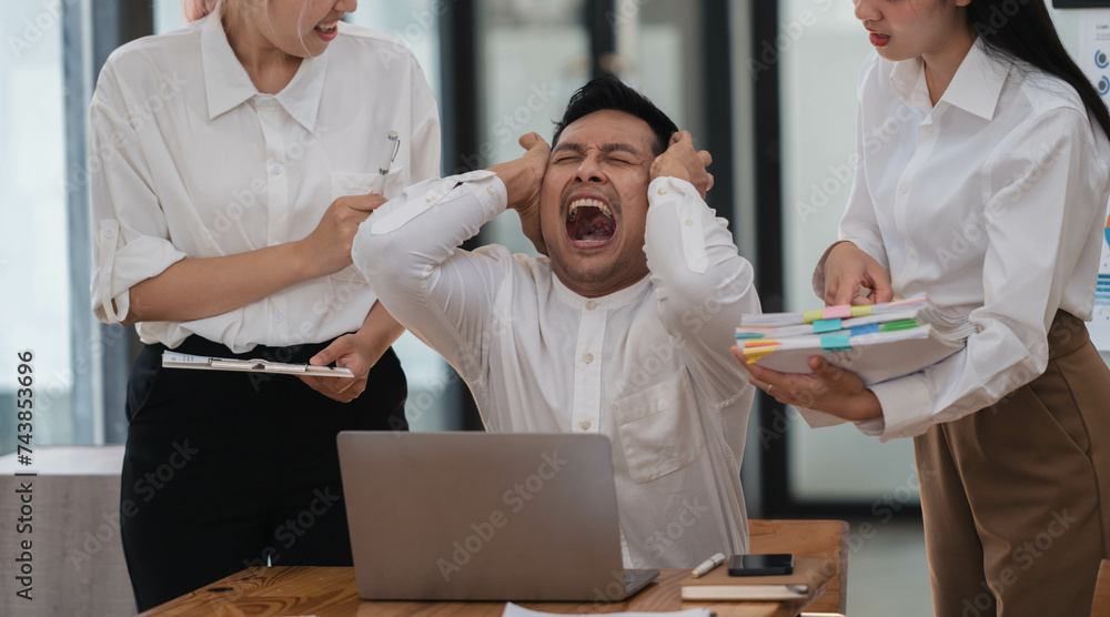 Obraz premium Frustrated Asian employee feels stressed suffers from hostile coworkers.