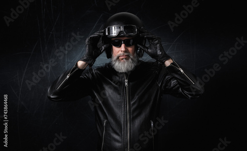 Portrait d'un biker motard homme avec un casque noir et une veste en cuir et des lunettes de protection et une barbe grise vintage