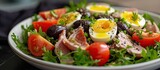 A traditional French Nicoise salad served in a white bowl, complete with a medley of fresh vegetables and topped with hard boiled eggs.