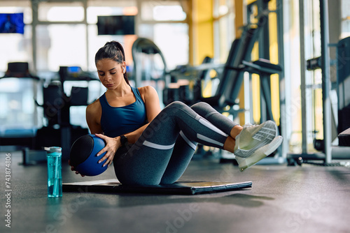 Young athletic woman using medicine ball while doing sit-ups during sports training in gym.