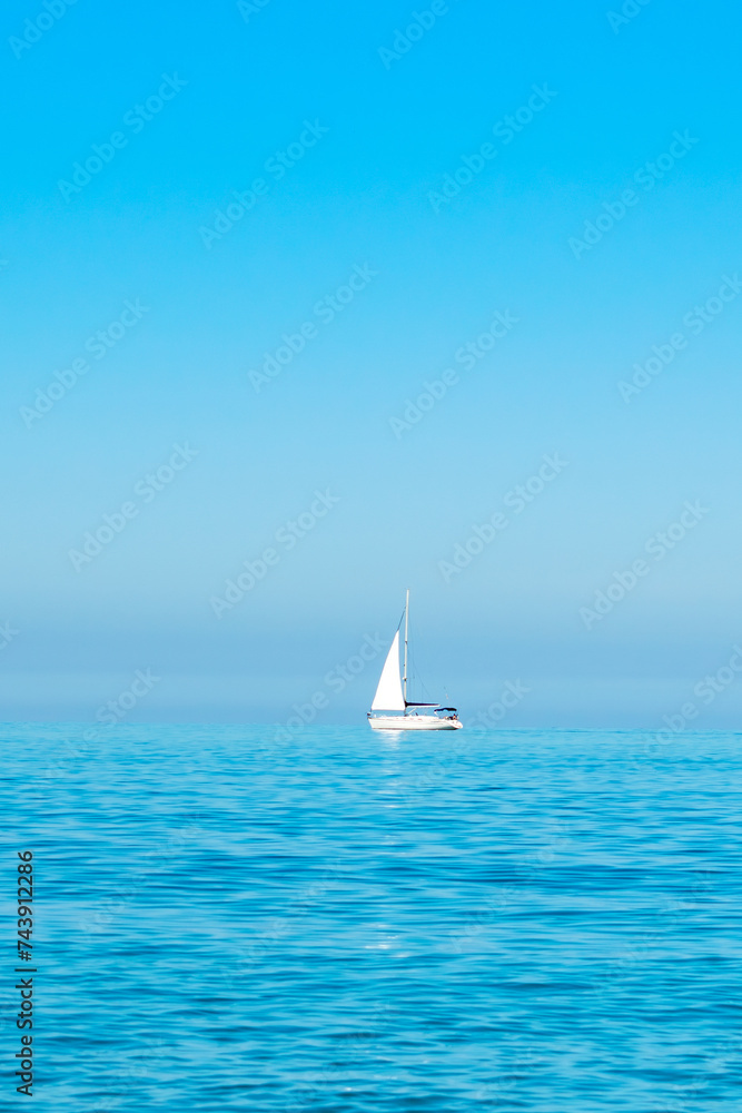Obraz premium white sailboat on the open sea near the horizon against a cloudless sky. Boat trip. place for text