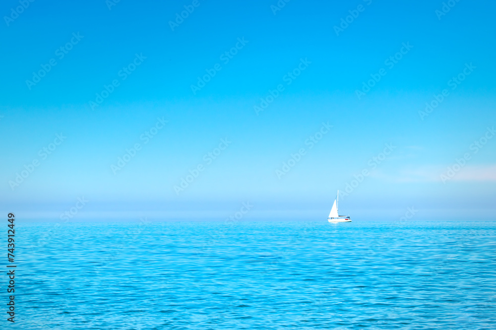 white sailboat on the open sea near the horizon against a cloudless sky. Boat trip. place for text