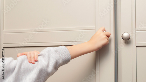 Child's hand opens the closet door. Cute baby girl playing with a wooden cupboard. Toddler baby opens the closet door in the home living room