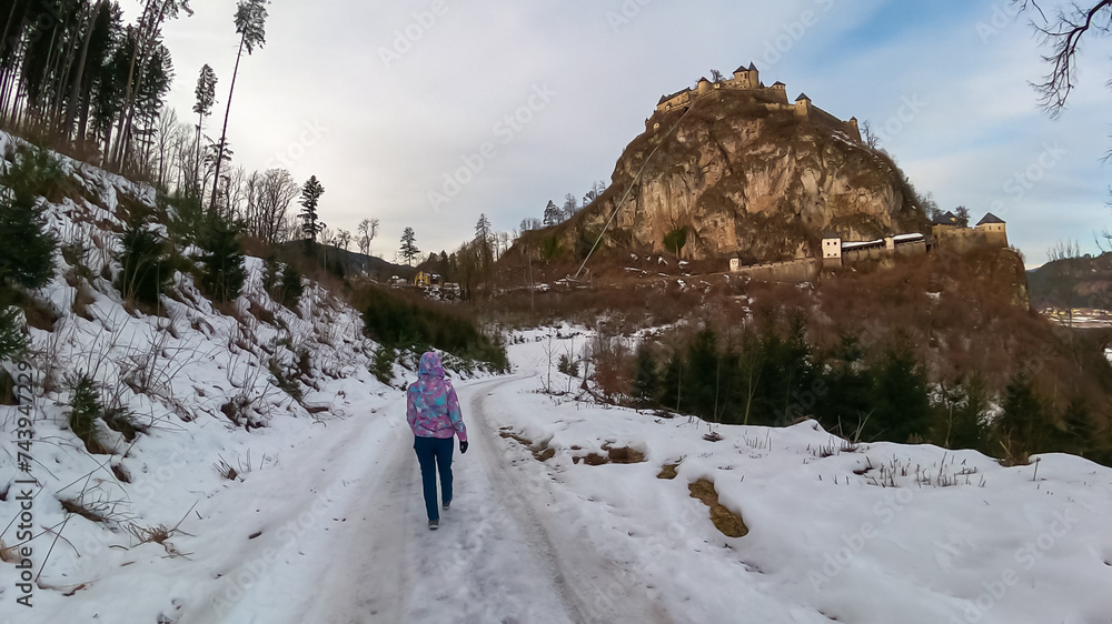 Tourist woman on snow covered hiking path leading to medieval castle Burg Hochosterwitz build on massive rock on a hill in Sankt Georgen am Längsee, Sankt Veit an der Glan, Carinthia, Austria. Winter