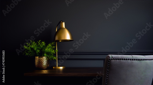 A golden lamp and a green plant on a wooden table with a gray chair in the background against a dark gray wall.