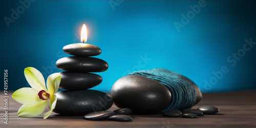 Black stones, orchid, and candle on a blue background.