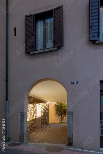 Arched entrance of an old renovated courtyard house with a beam of light illuminating the entrance corridor. A plant can be seen at the bottom