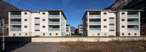 Front view of a residential complex with the garden and games for children. There is blue sky.