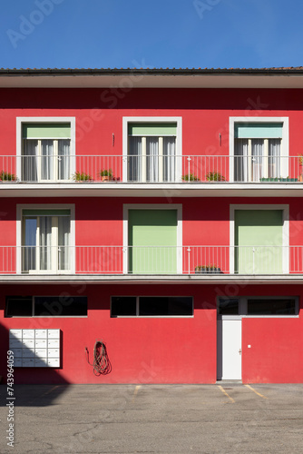 Detail of a red railing house with parking below. There is a letterbox for the entire condominium and a closed white door.