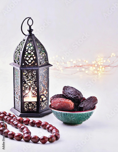 Concept of Ramadan food and beverages. Arabian lantern, wooden rosary, dates fruit, and illumination against a white backdrop, symbolizing the essence of Ramadan.