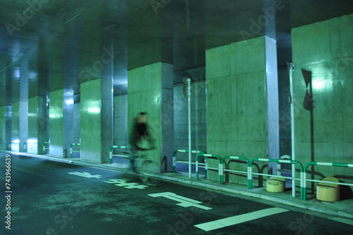 夜の光が反射しているトンネルを、「止まれ」の路面標識を踏み越えて駆け抜けるサイクリスト photo