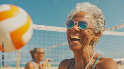 Senior woman laughing as she plays a game of beach volleyball with her friends on a sunny day photo