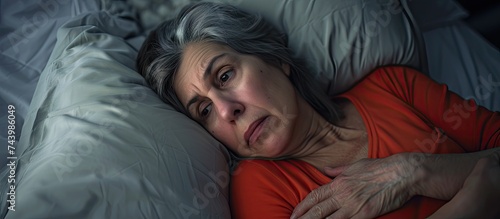 Middle aged woman sitting on bed feels unhealthy touch stomach suffers from severe crampy abdominal pain. with copy space image. Place for adding text or design photo
