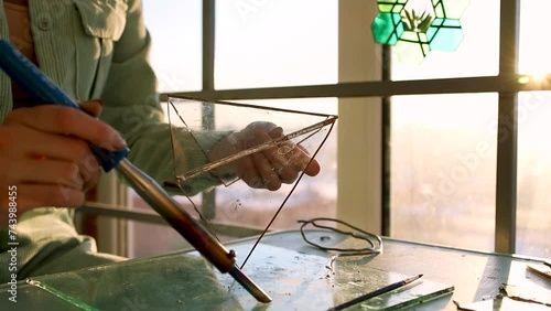 Girl with a soldering iron in her hands soldering a glass stained glass triangle