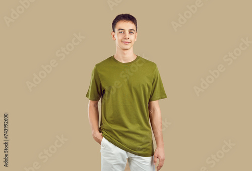 Confident smiling peaceful young boy student wearing casual clothes isolated on a studio beige background. Smart guy looking at camera indoors. People portrait and emotions concept.