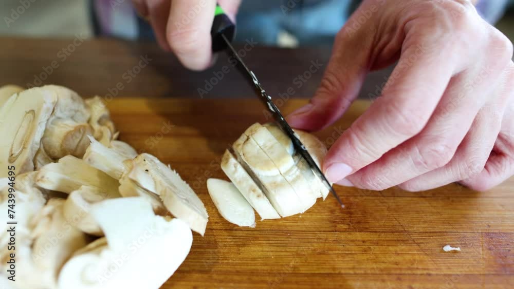 A woman prepares food in the kitchen at home. Slices mushrooms with a knife on a cutting board A woman prepares food in the kitchen at home. Slices mushrooms with a knife on a cutting board