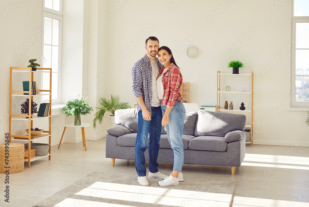 Full length portrait of a happy family couple stands together in cozy living room, embracing and sharing smiles. Joy, fun, and leisure, capturing the essence of togetherness in home. Full length portrait of a happy family couple stands together in cozy living room, embracing and sharing smiles. Joy, fun, and leisure, capturing the essence of togetherness in home.