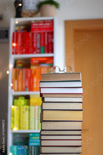 High stack of books on the table. Colorful rainbow bookshelf in the background. Selective focus.