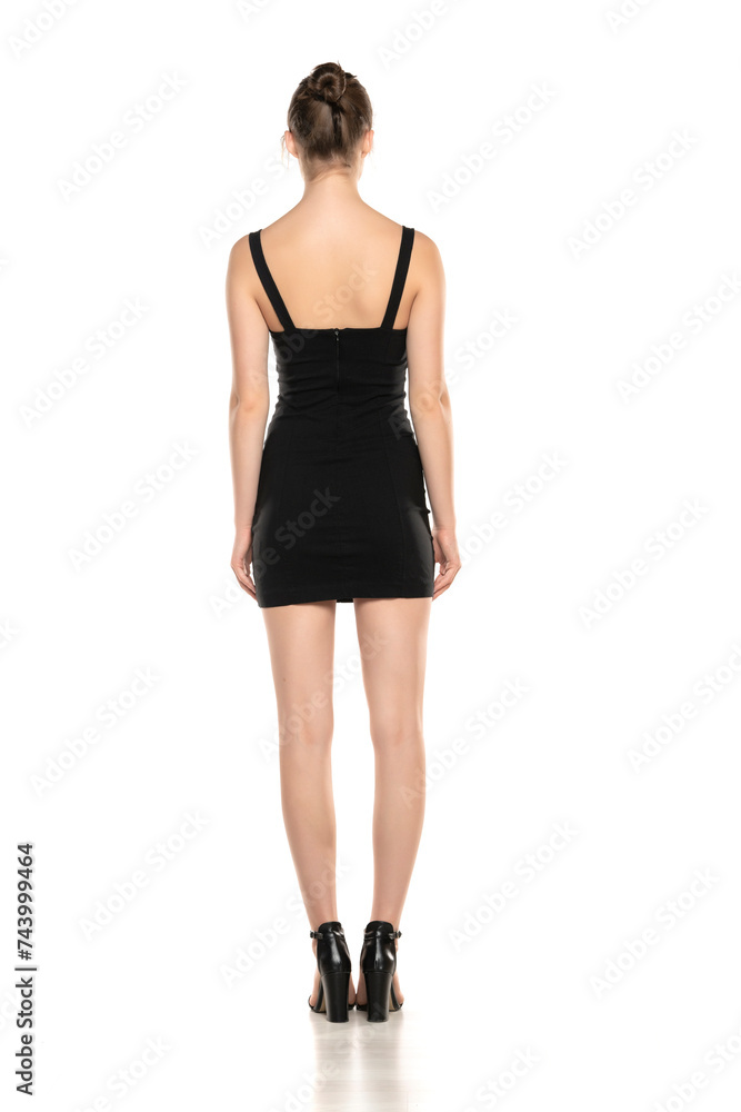 Back View Elegance: Rear Portrait of a Young Woman in a Short Dress and High Heel Sandals on White Background Back View Elegance: Rear Portrait of a Young Woman in a Short Dress and High Heel Sandals on White Background