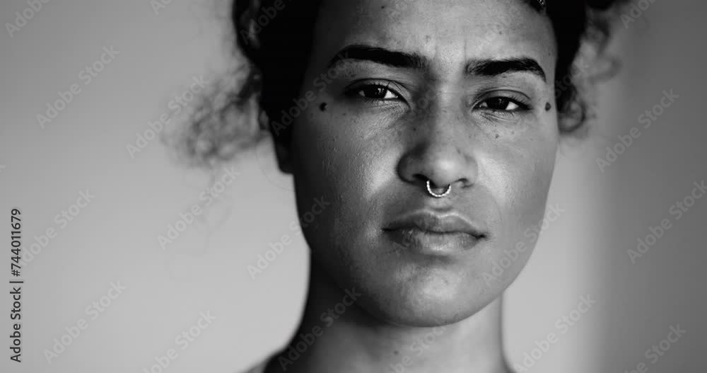 Serious African American young woman staring at camera in monochromatic portrait. Close-up face of a stern solemn black adult girl in 20s in dramatic black and white Serious African American young woman staring at camera in monochromatic portrait. Close-up face of a stern solemn black adult girl in 20s in dramatic black and white