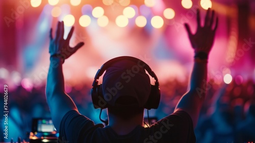 Closeup of the back of a DJ man in neon lights with her hands raised up greets dancing and relaxing people in a nightclub photo