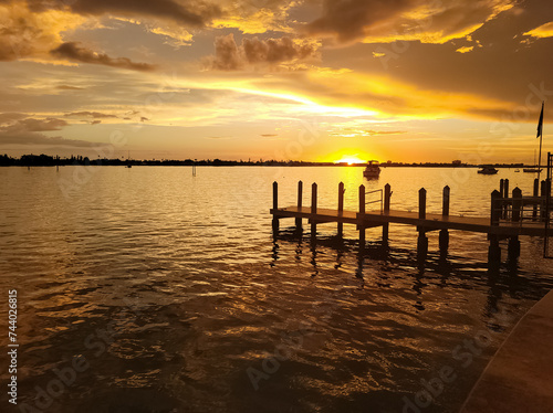 An image of a colorful sunset over the bay near Treasure Island  Floridia with a wooden dock in the foreground.