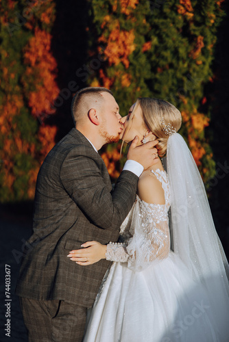 A young bride and groom tenderly embrace in the rays of the autumn sun. Tender and beautiful young girl bride. A man kisses his beloved. Against the background of a beautiful garden