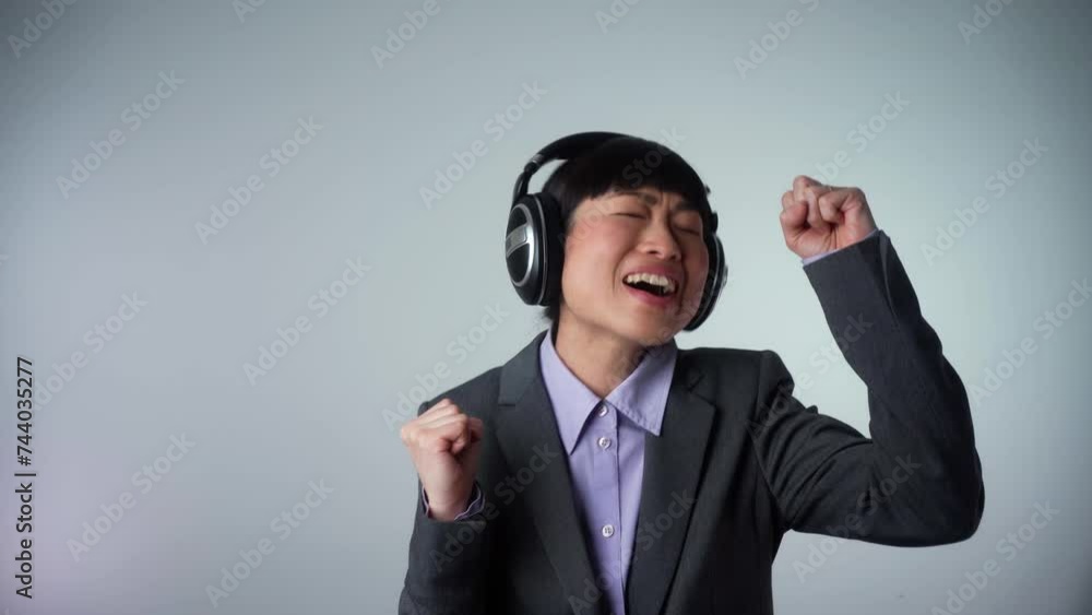 Cheerful Asian business woman posing isolated on grey wall background studio, medium shot. 4k video footage. People lifestyle concept. Mock up copy space. Listen music with headphones, dancing Cheerful Asian business woman posing isolated on grey wall background studio, medium shot. 4k video footage. People lifestyle concept. Mock up copy space. Listen music with headphones, dancing