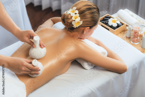 Hot herbal ball spa massage body treatment, masseur gently compresses herb bag on woman body. Tranquil and serenity of aromatherapy recreation in day lighting ambient at spa salon. Quiescent
