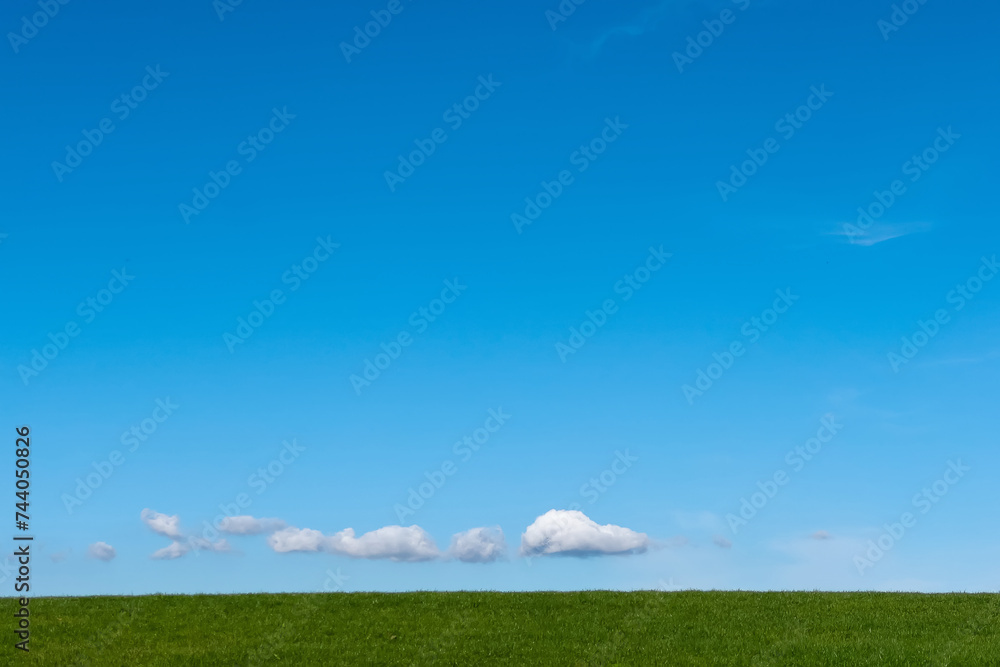 Fototapeta premium Small clouds over horizon over green grass hill