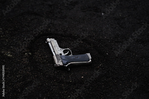 A gun lying on black sand, hand gun and bullets, close up of a gun © SN_Creation
