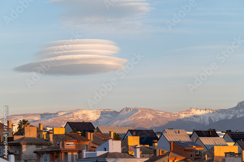 Spectacular lenticular clouds over houses and snowy mountains in the background at sunset in Granada (Spain)