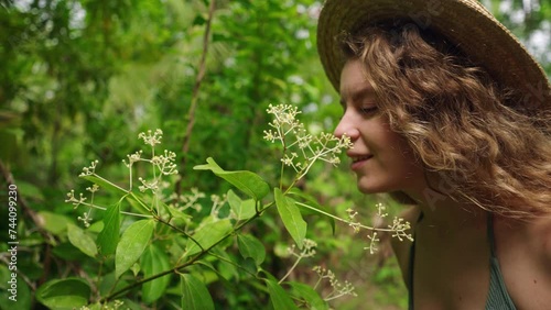 Woman examines and smells white cinnamon flowers in a lush green botanical garden, immerse in natural plant aromas, peaceful and tranquil nature moment, naturalist enjoys flora scent.