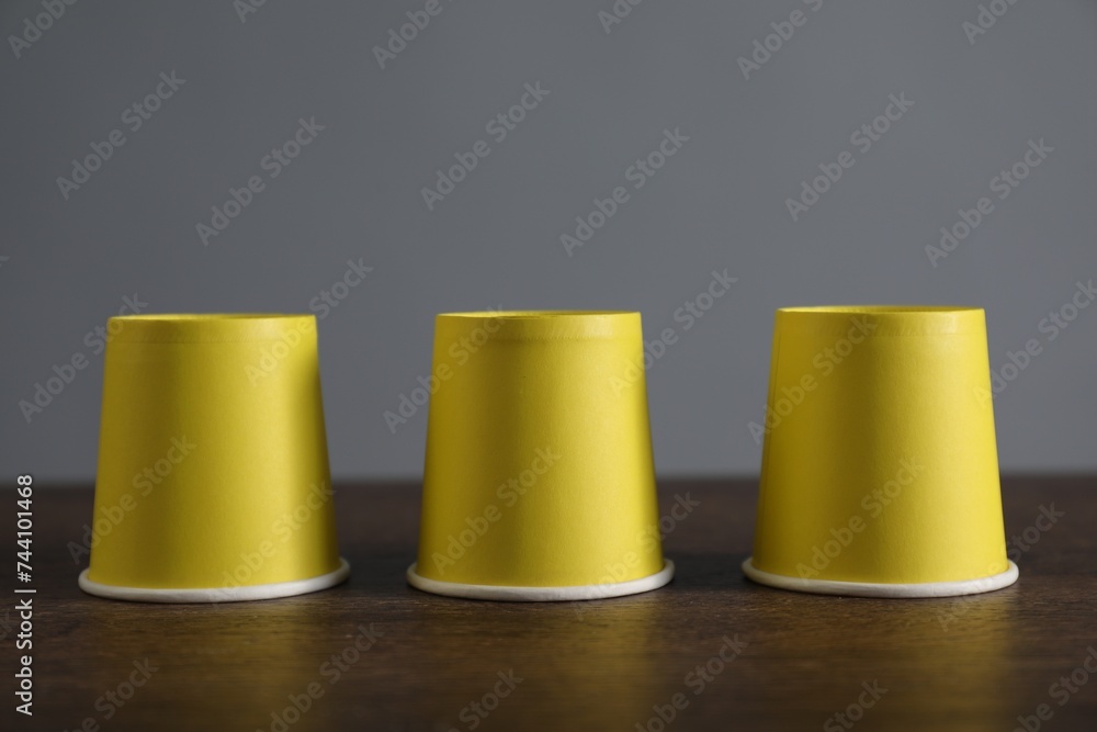 Shell game. Three yellow cups on wooden table Shell game. Three yellow cups on wooden table