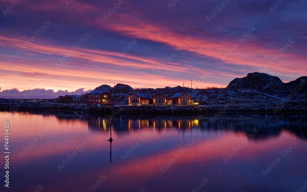 Sunrise reflection on the clouds above small island with some cabins on. Lofoten Islands, Northern Norway. 