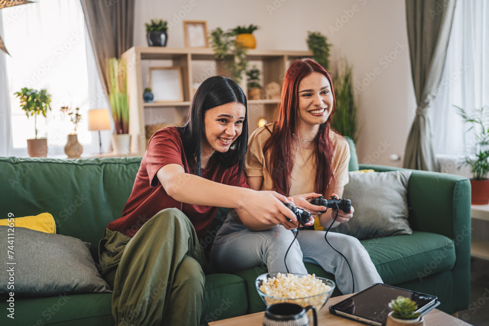 Two young women caucasian friends or sisters play console video game