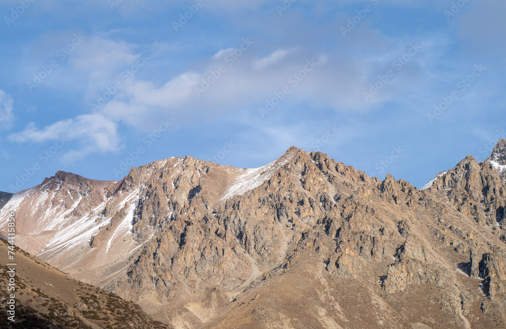Tall beige cliffs are covered with a slight snow cover..Beige mountains without vegetation in autumn, blue sky. Tall beige cliffs are covered with a slight snow cover..Beige mountains without vegetation in autumn, blue sky.