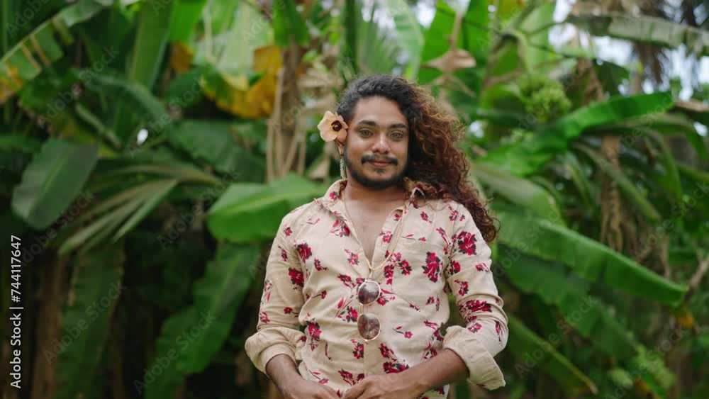 Flamboyant male with flower hairpiece strikes poses in floral shirt, denim shorts amidst lush greenery. Effeminate man models confidently, eyes adorned by striking contacts, exuding pride, diversity. Flamboyant male with flower hairpiece strikes poses in floral shirt, denim shorts amidst lush greenery. Effeminate man models confidently, eyes adorned by striking contacts, exuding pride, diversity.