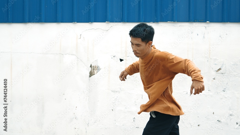 Hispanic man stretch arms and dance break dancing in front of wall. Motion shot of stylish street dancer in casual outfit practicing dancing in hip hop style. Outdoor sport 2023. Background. Endeavor.
