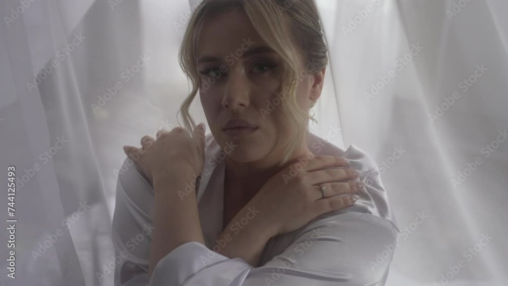 A woman in a white shirt stands by the window, hand on jaw A woman in a white shirt stands by the window, hand on jaw