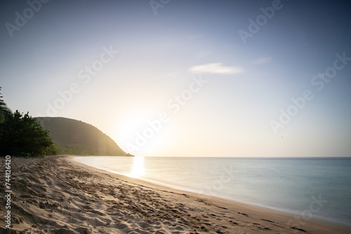 Guadeloupe, a Caribbean island in the French Antilles. View over Grande Anse beach. Lonely bay, feet in the sand and looking out to sea at sunset. Landscape shot of a tropical dream, waves, palm trees © Jan