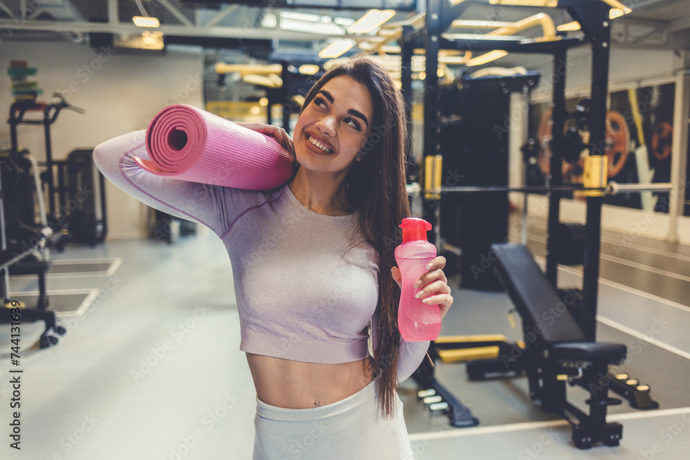 Fototapeta premium Fit body, healthy and athletic woman in the gym holding mat and water bottle for yoga, pilates or exercise. Portrait of sporty, active or slim athlete ready for workout or training.