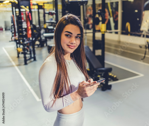 Idea, phone and exercise with a sports woman by a window, standing in the gym during a fitnesss workout. Health, thinking and a female athlete using social media or an app to track her training. photo