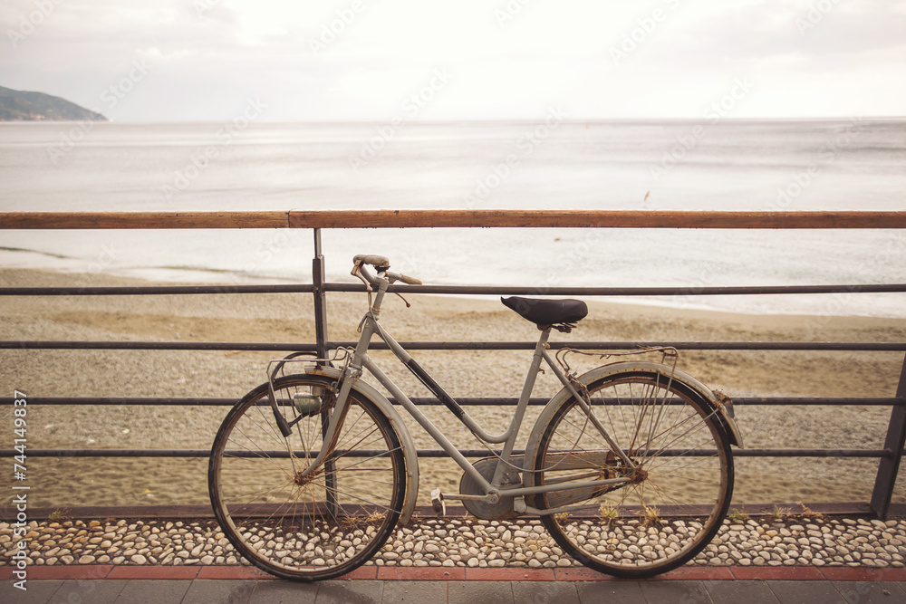 bicycle on the beach in the morning. A bicycle stands at a metal railing against the background of the sea. Bicycle in front of a beach at Mediterranean seashore in Italy.